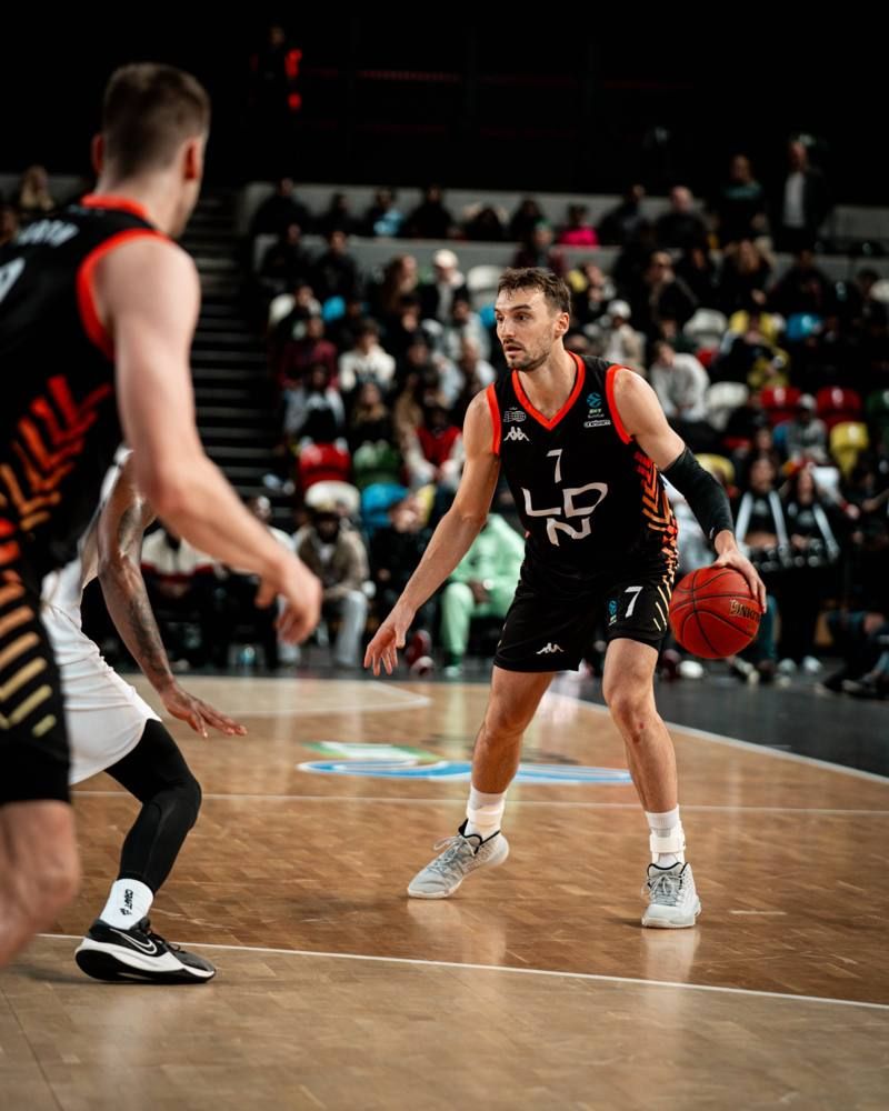 A London Lions player in the black and orange LDN kit dribbles in front of a full crowd